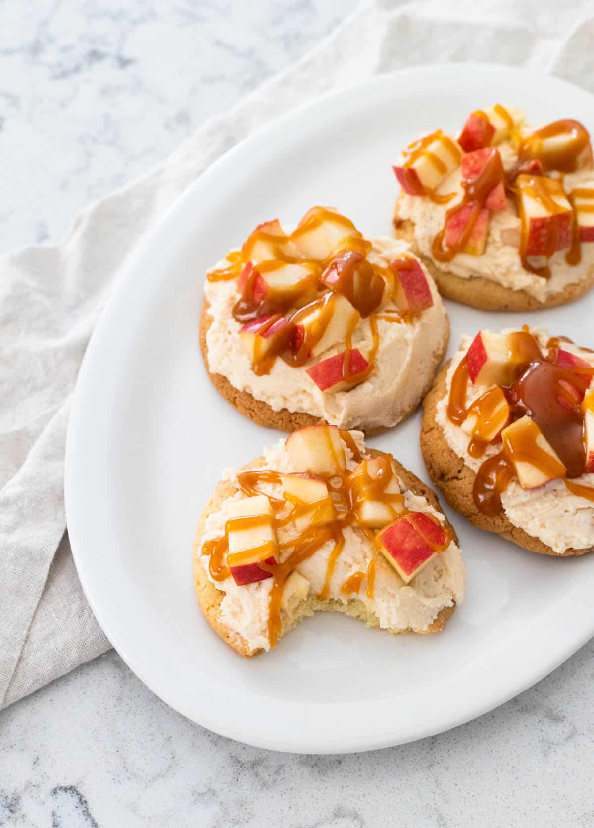 The cookies topped with fresh apples and caramel have been served on a white platter.