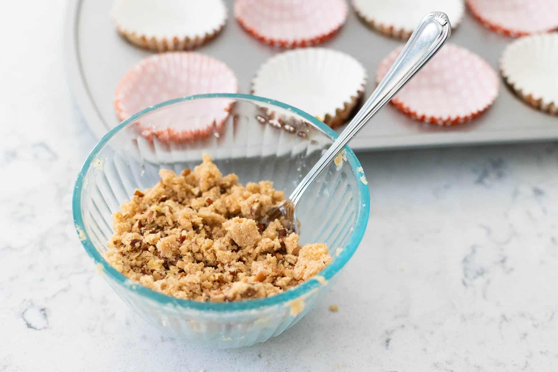 A mixing bowl filled with brown sugar and cinnamon streusel sits in front of the muffin pan.