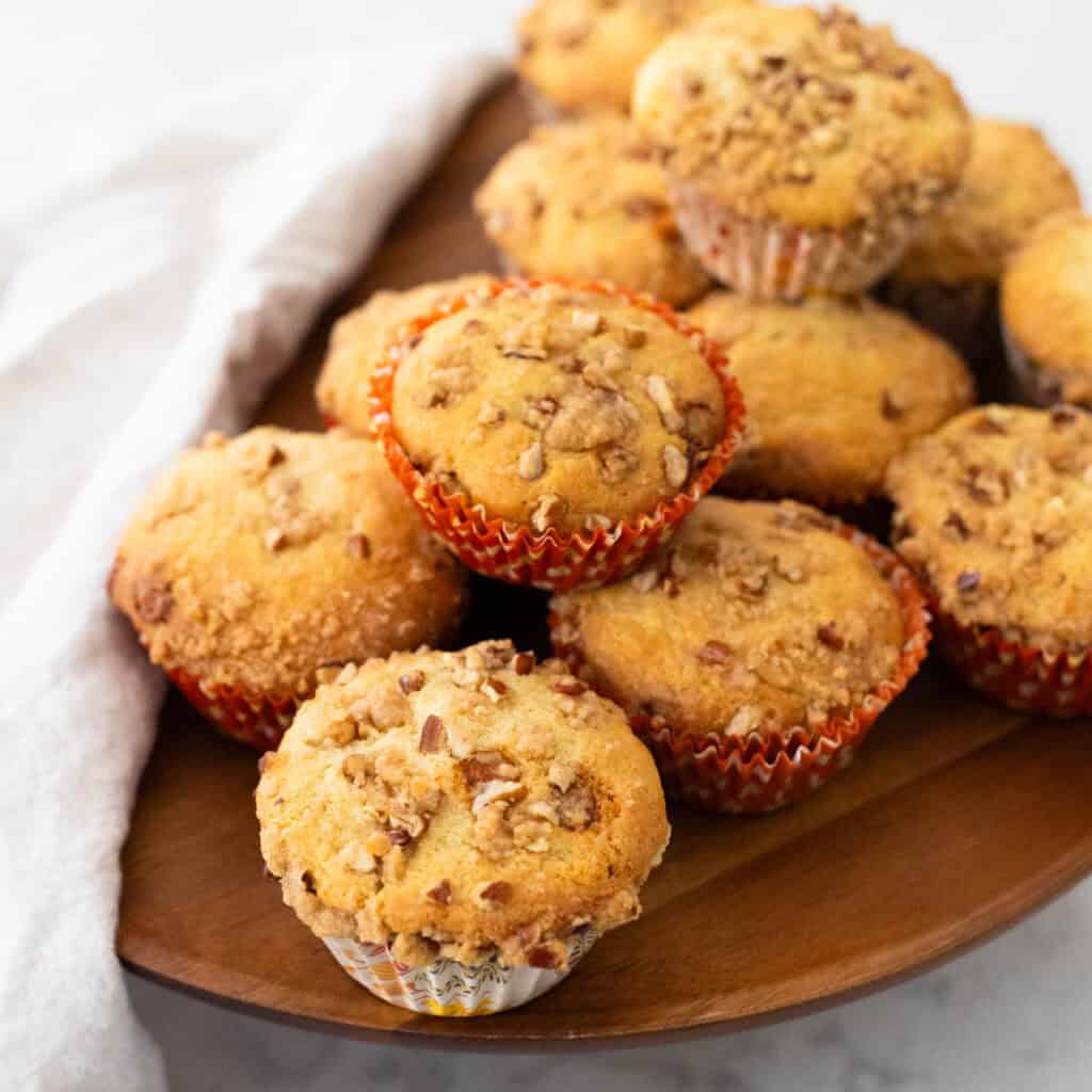 A pile of muffins with cinnamon streusel topping sit on a serving platter with a napkin draped on the side.