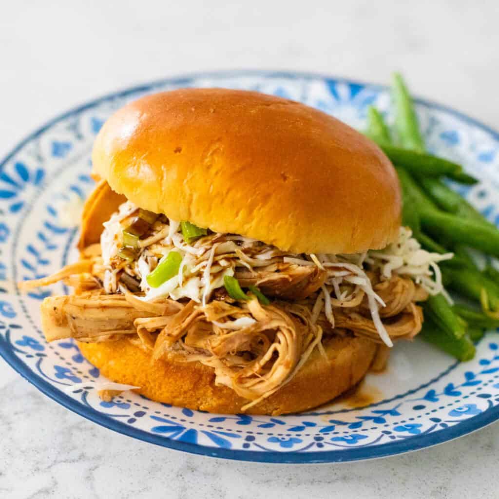 The shredded chicken sandwich has slaw and green onions on top, a serving of green beans on the side.