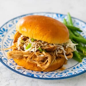 The shredded chicken sandwich has slaw and green onions on top, a serving of green beans on the side.