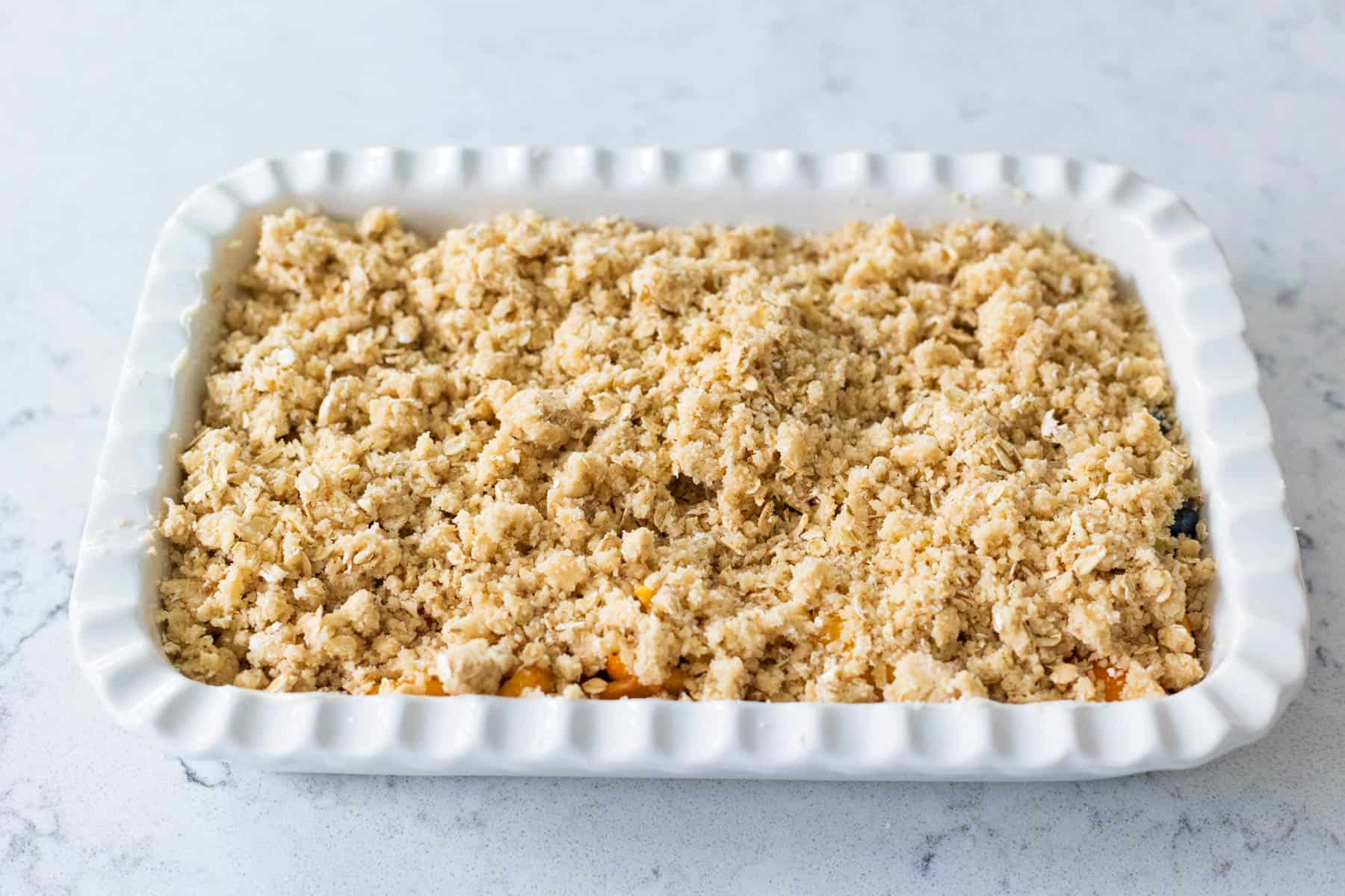 The buttery crisp topping has been spread evenly over the top of the fruit filling in the baking dish.