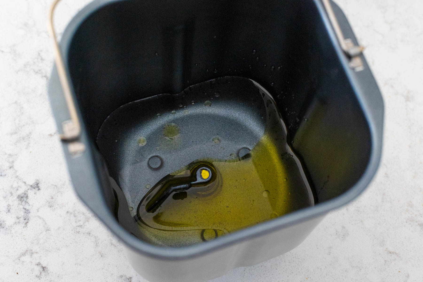 The bread machine pan has the olive oil and water.