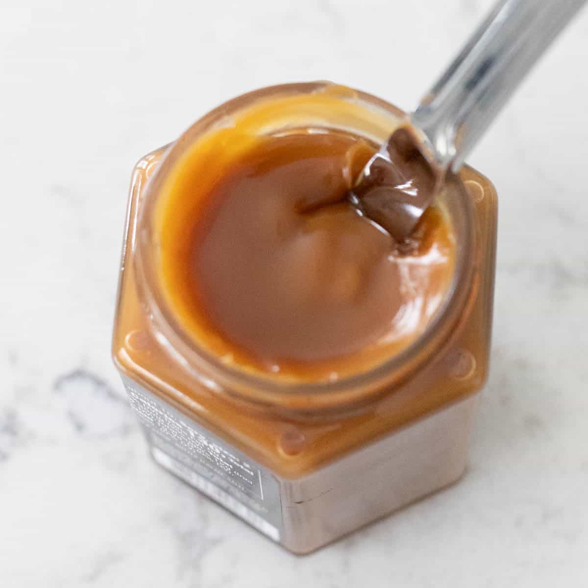 The jar of caramel sauce has been heated in the microwave so that it is soft and pliant.