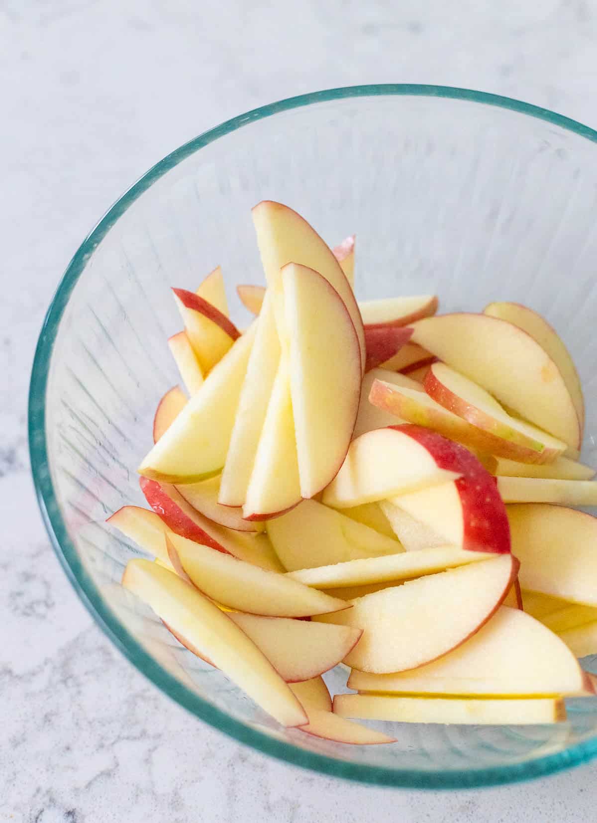 The fresh apples have been sliced and tossed with lemon juice in a mixing bowl.