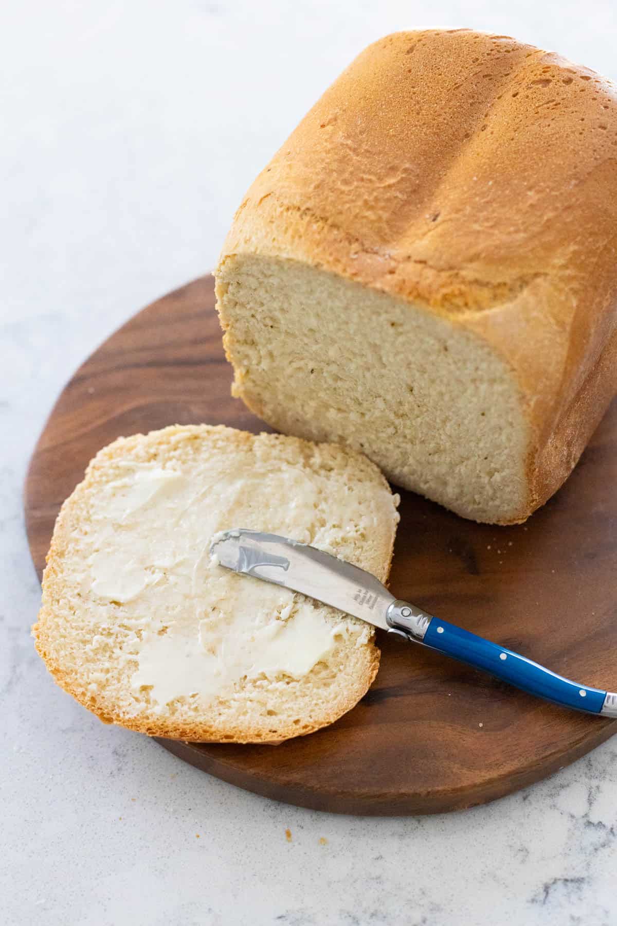 The bread has a slice in front of it being spread with butter.