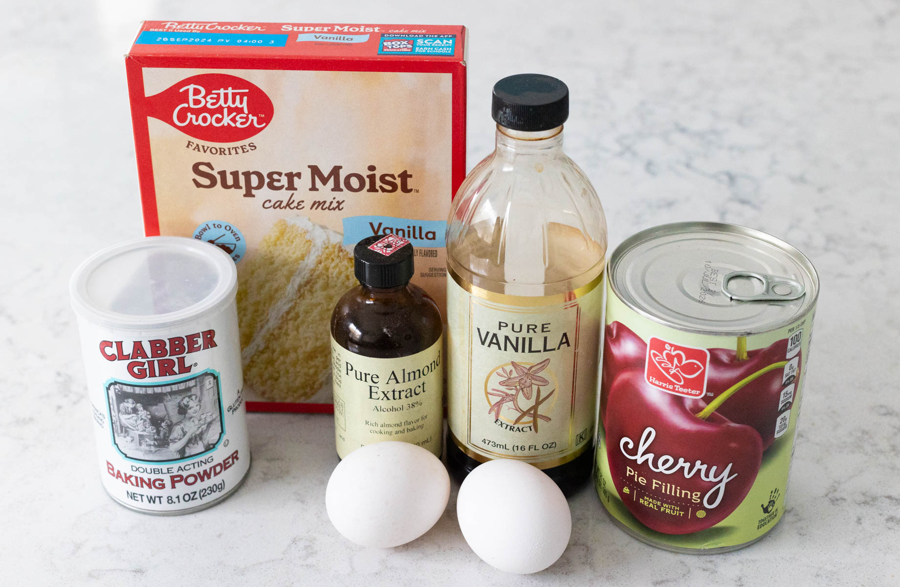 The boxed cake mix, can of cherry pie filling, and other ingredients to bake the cherry cake are on the counter.
