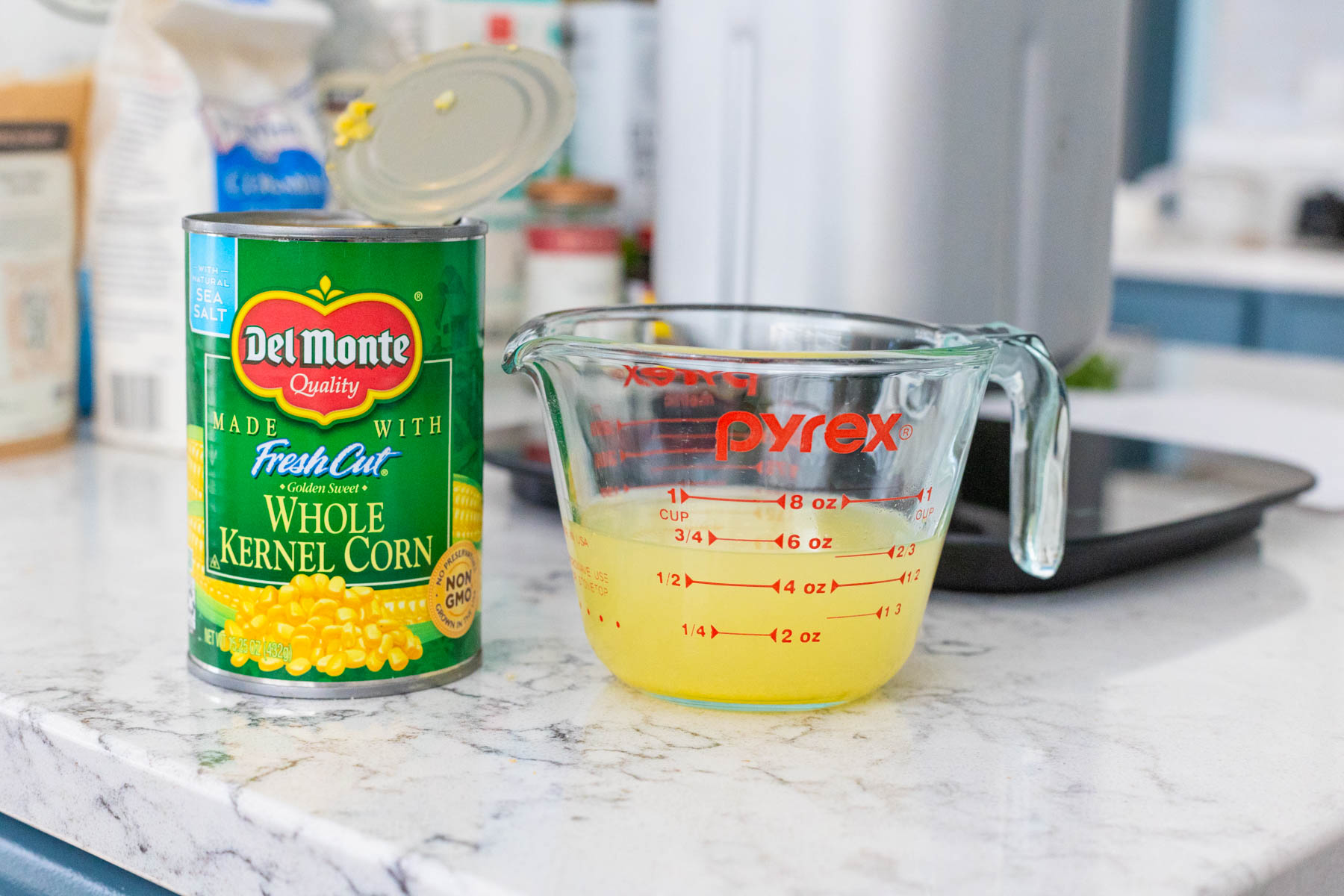 The can of corn is next to a measuring cup filled with the packing liquid.
