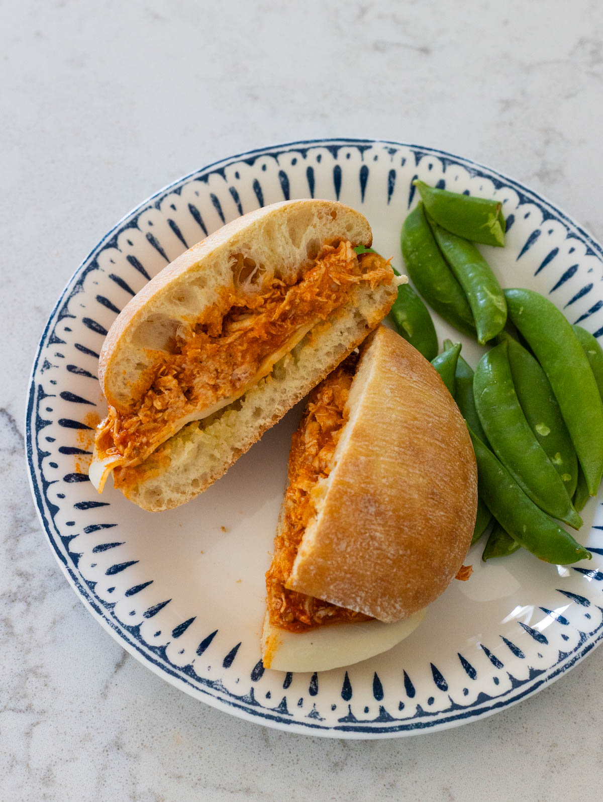 The chicken sandwich has been cut in half so you can see the filling. It is on a plate with fresh pea pods.