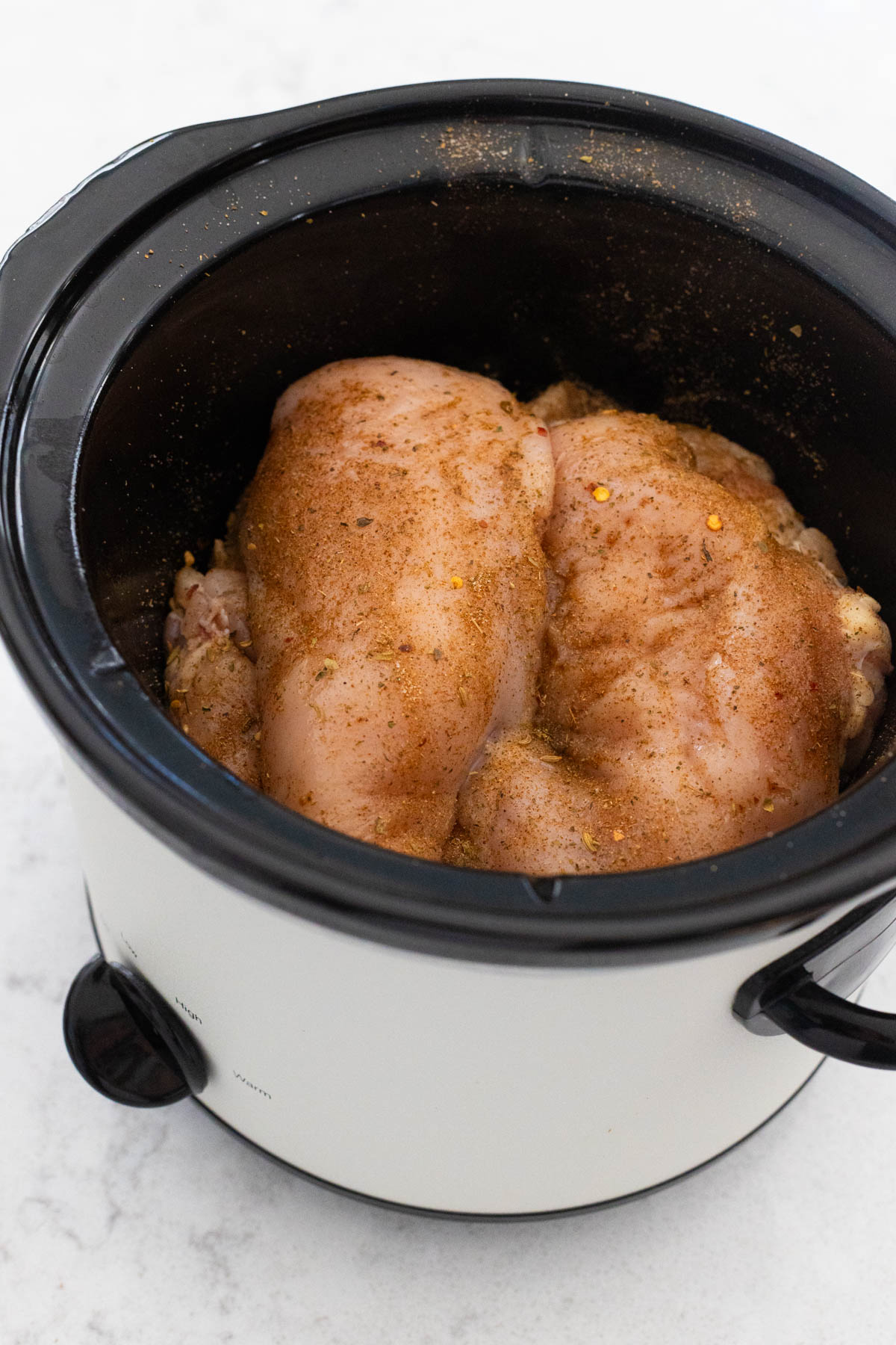 The chicken breasts are in the slowcooker and have had seasoning sprinkled over the top.