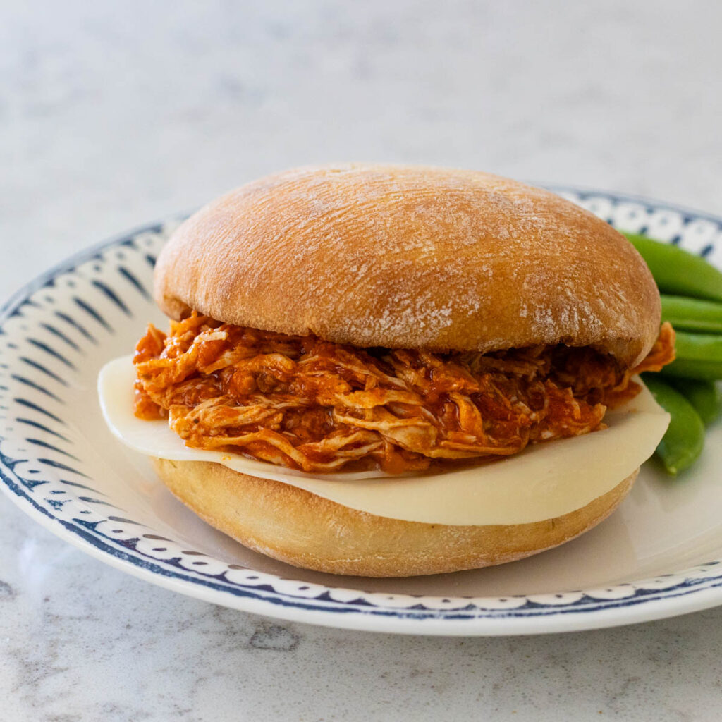 A tomato sauce and shredded chicken sandwich has provolone cheese on a crusty bun.