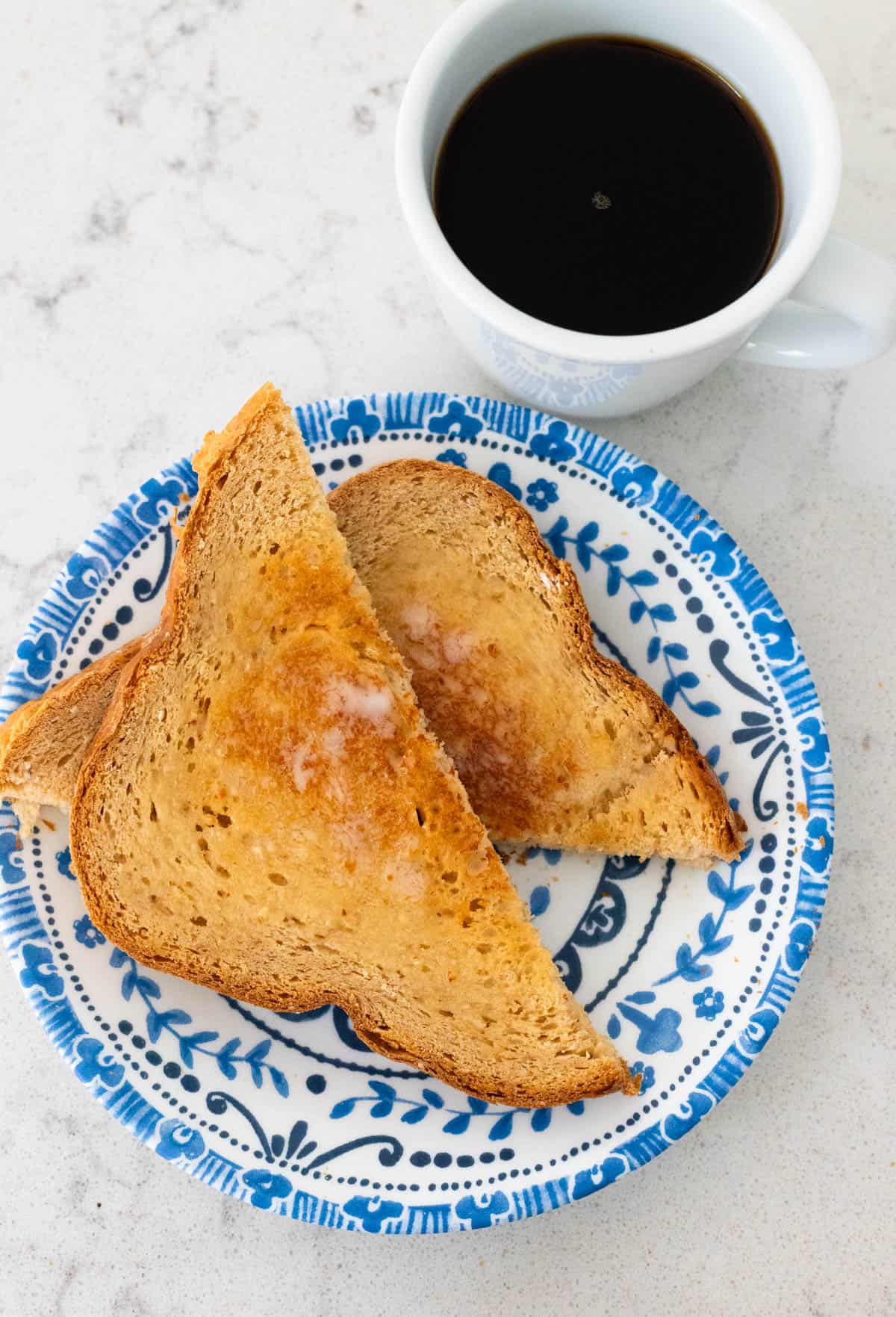 The bread has been sliced and toasted. It is served on a blue plate with a mug of coffee.