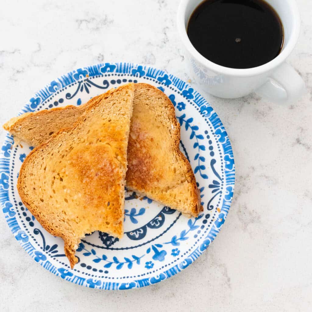 A piece of toast has been sliced into triangles and served on a blue plate next to a mug of coffee.