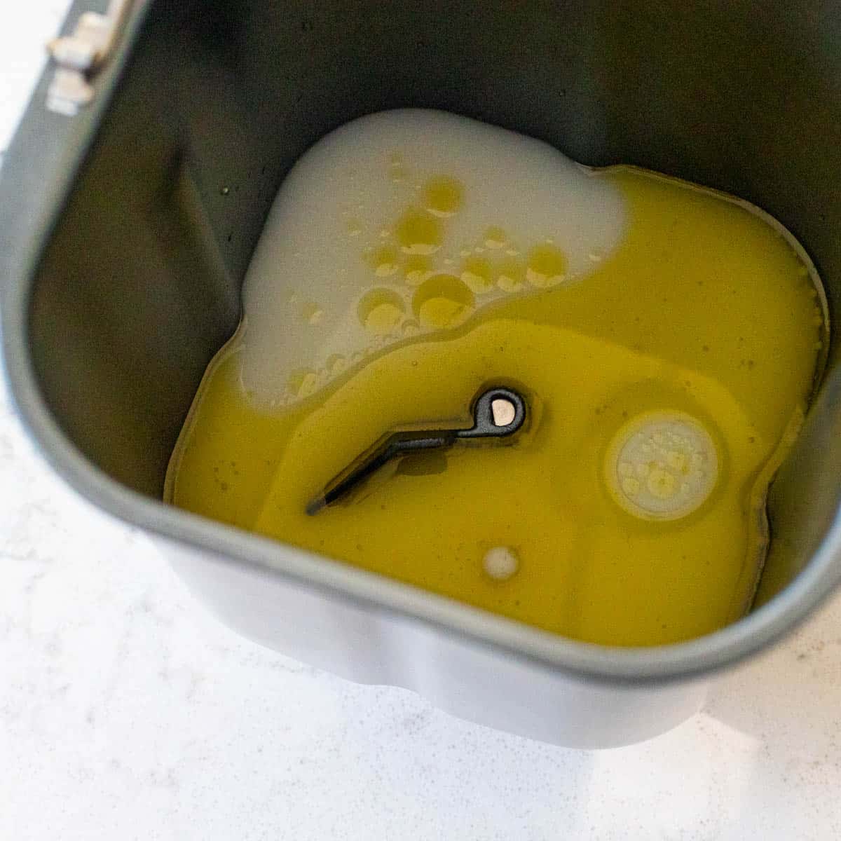 The wet ingredients have been added to the bread machine pan.