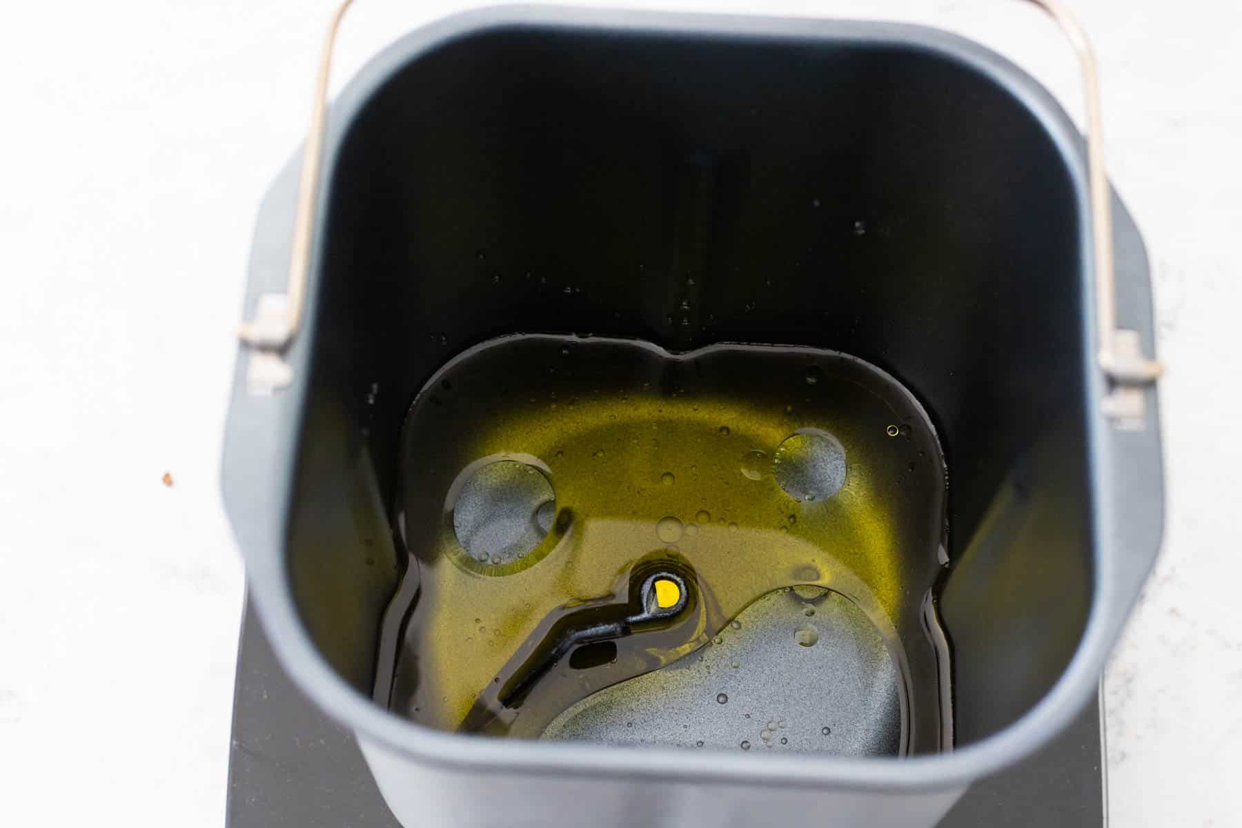 The olive oil and water are inside the bread machine pan.