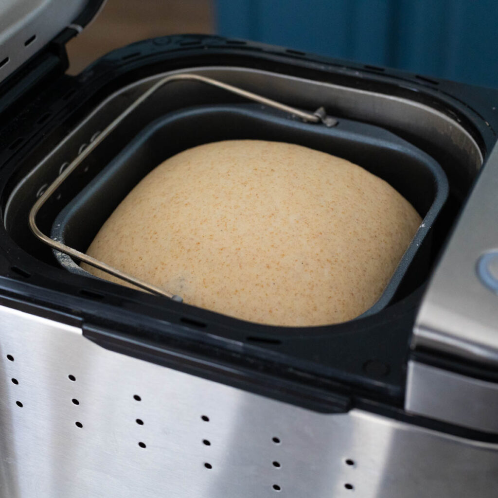 The risen pizza dough is inside the bread maker.