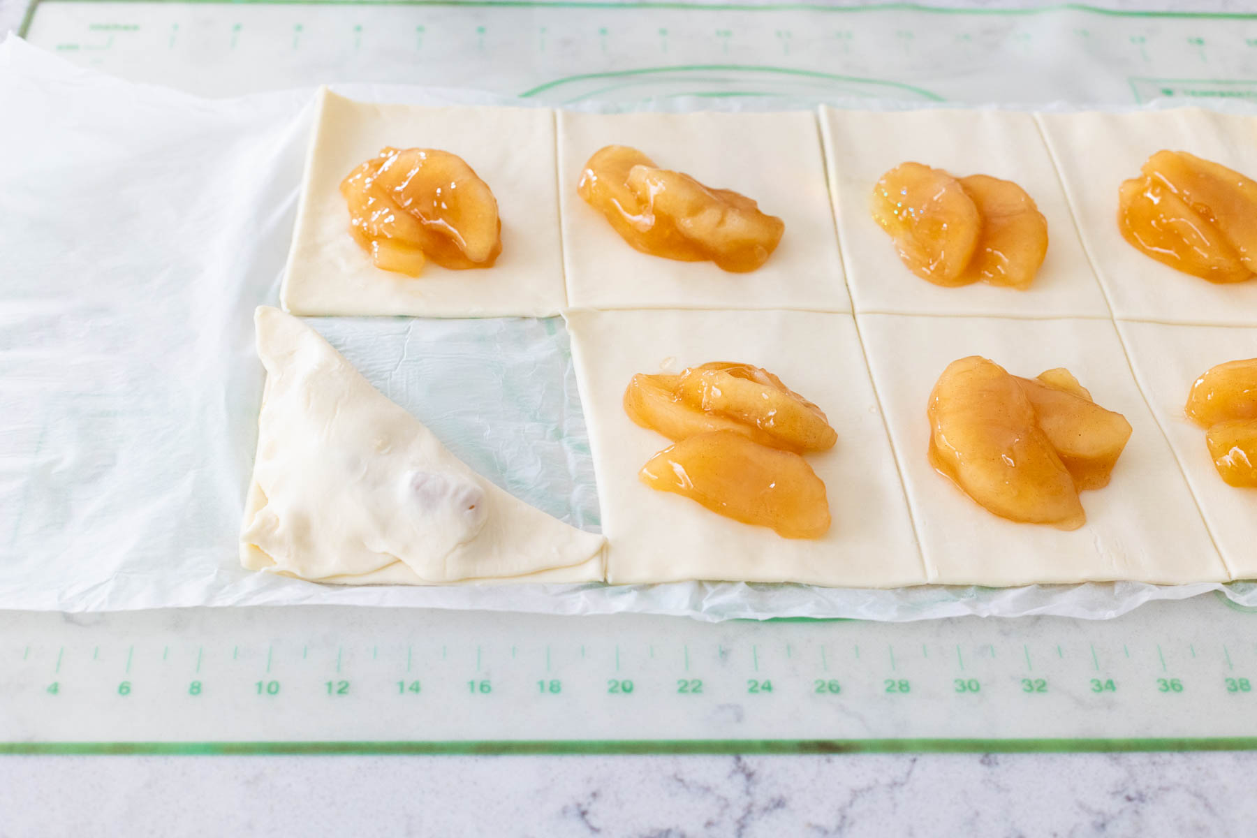 The apple pie filling has been spooned onto each pastry square.