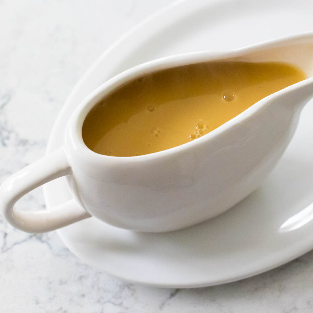 A gravy boat filled with chicken gravy on a white platter.