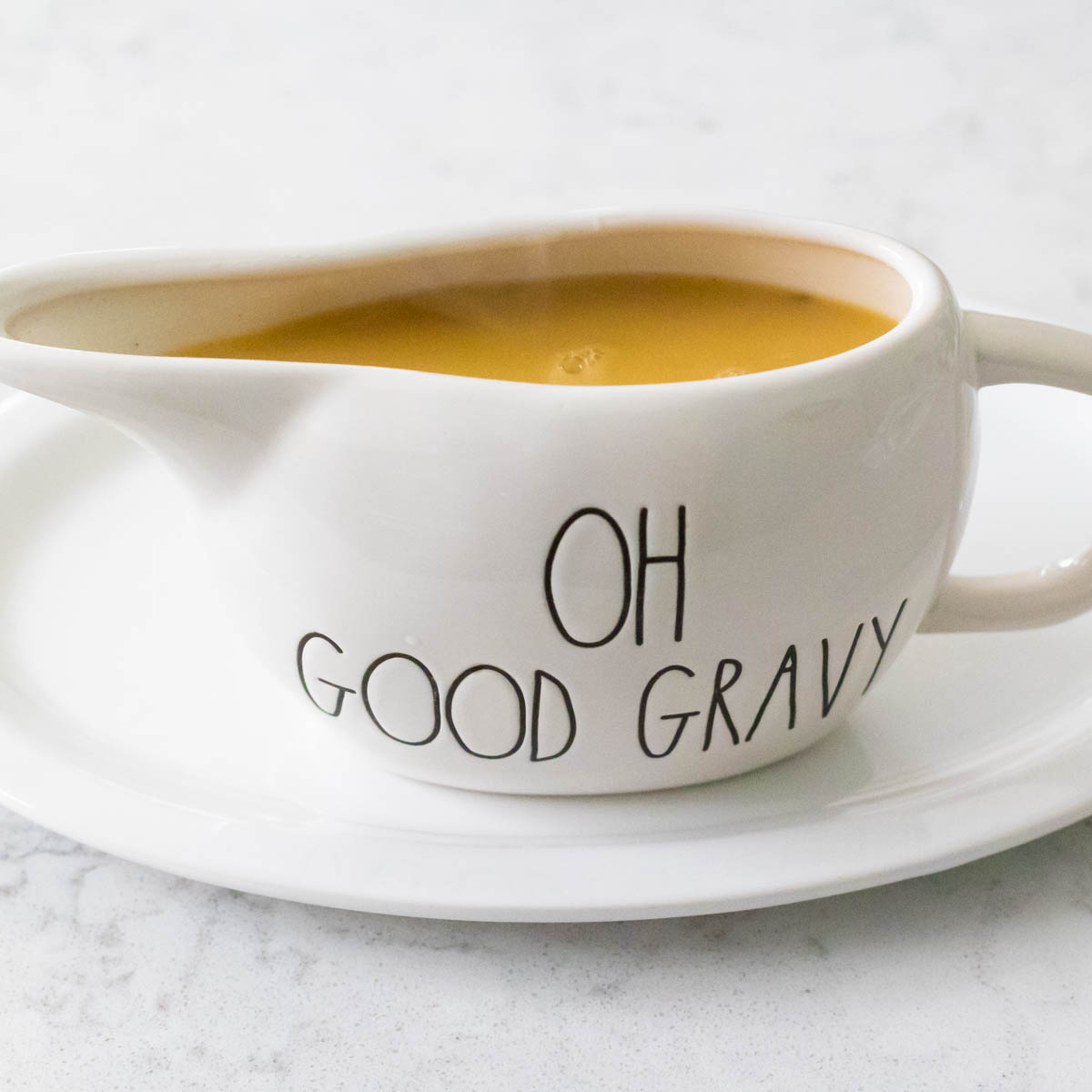 A gravy boat that says "Oh Good Gravy" is filled with chicken gravy on a white platter.