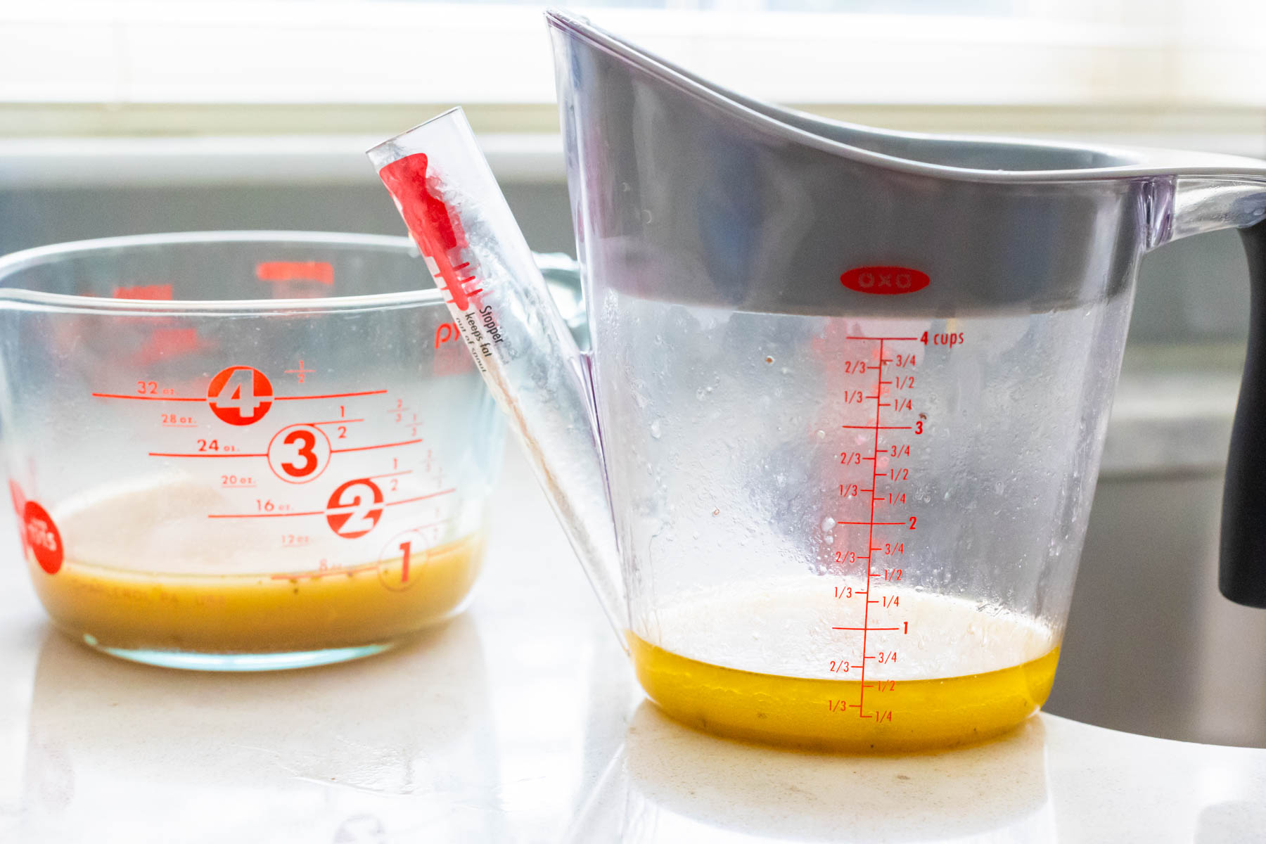 The fat separator filled with chicken fat sits next to a measuring cup with the cooking liquid.