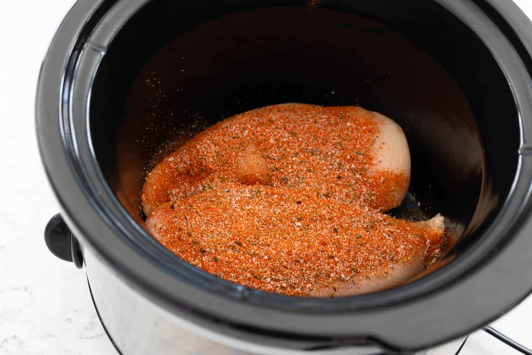 The chicken breasts have been sprinkled with Cajun seasoning inside a crockpot.