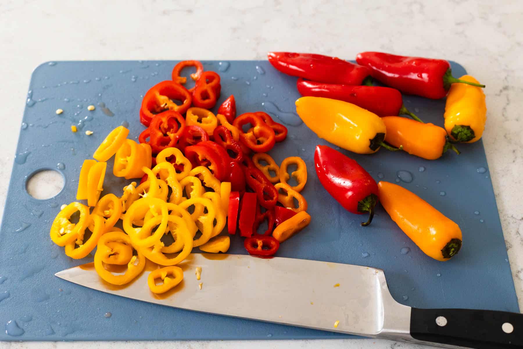 A cutting board is loaded up with mini peppers. One pile is whole, another pile has been sliced. 