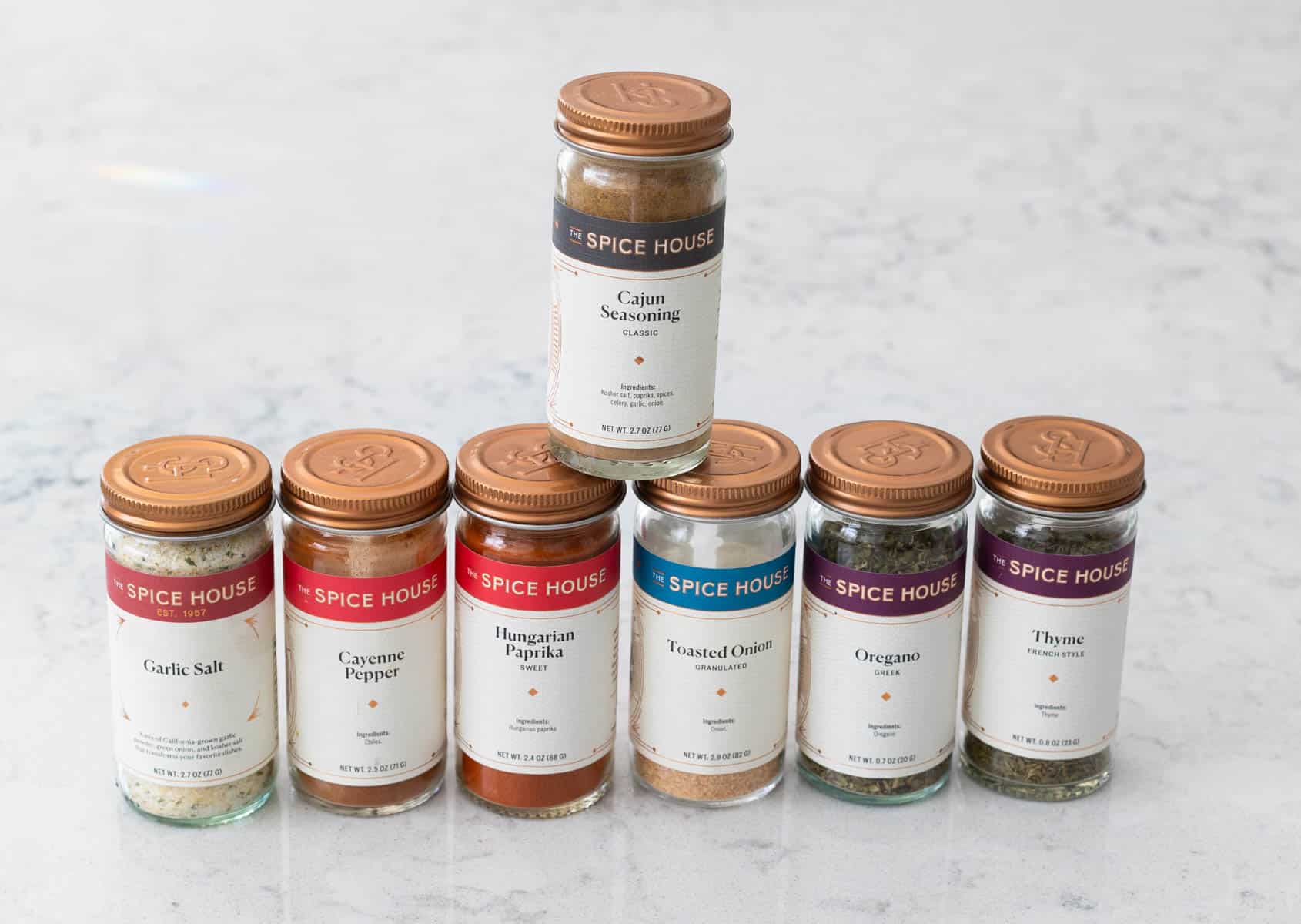 A row of spice jars that make up cajun seasoning blend sits on the bottom with one jar of cajun seasoning blend on top of the pile.