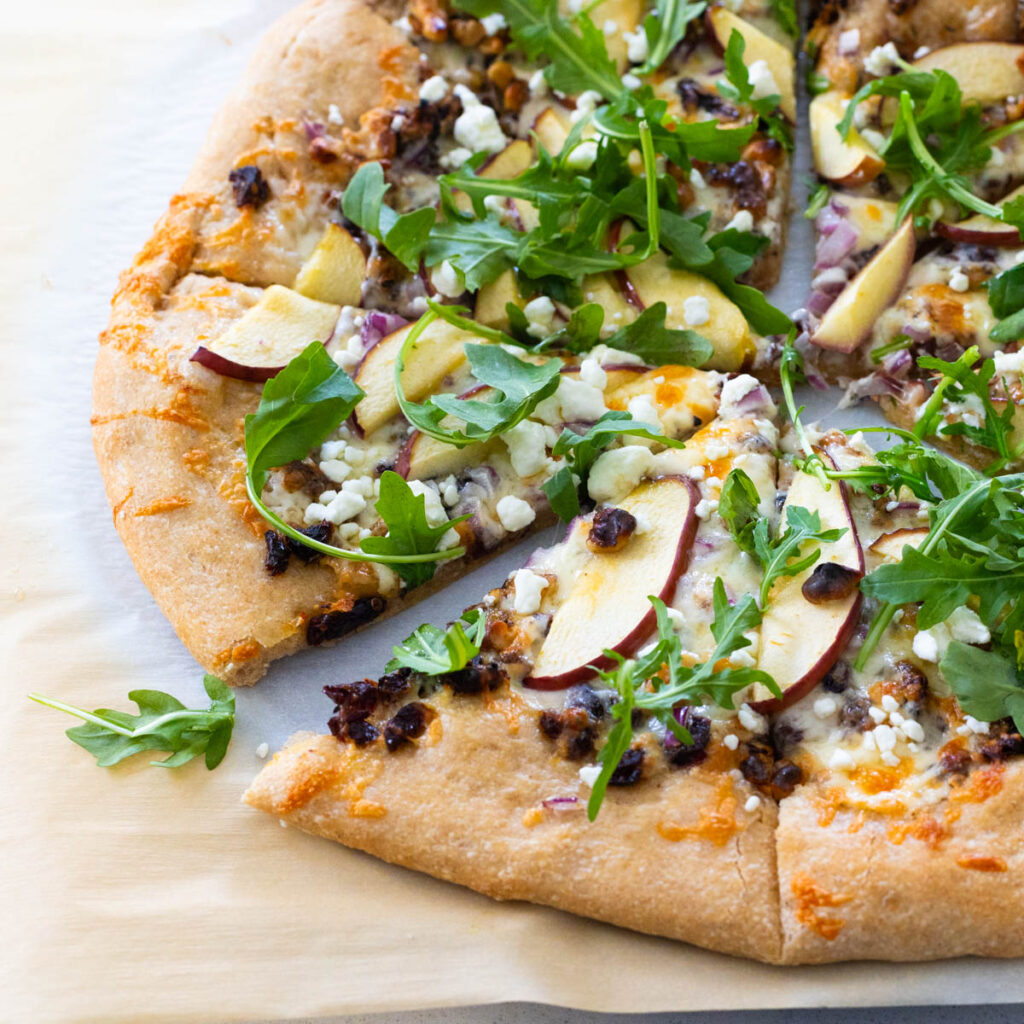 The finished savory apple pizza has a golden brown crust, sliced apples, and fresh arugula scattered over the top.