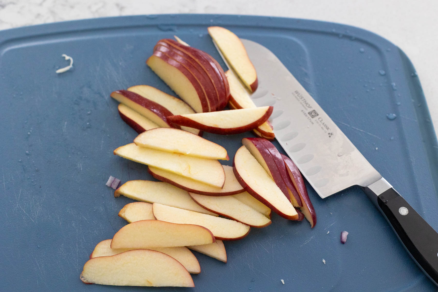The apple has been thinly sliced on a cutting board with a large knife.