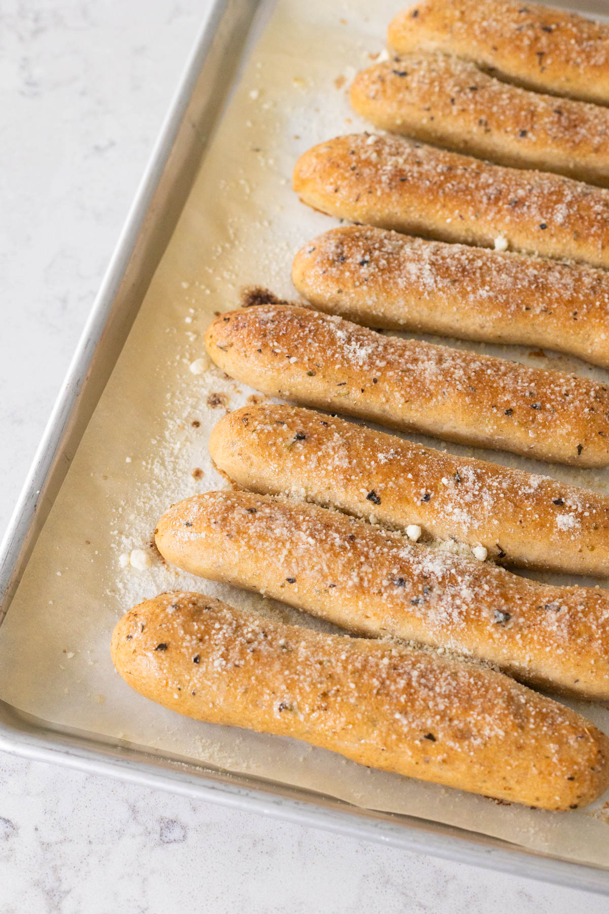 The grated parmesan has been sprinkled over the breadsticks on the baking pan.