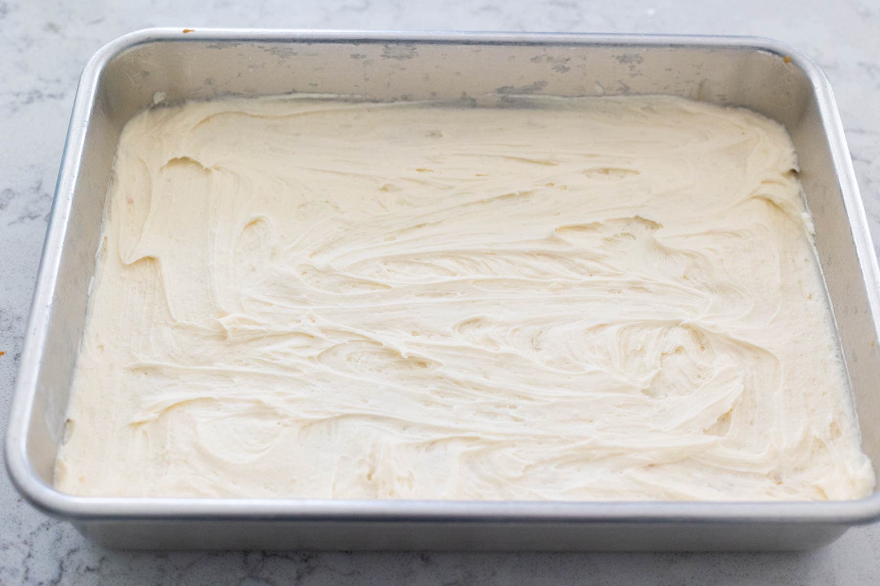 The pan of cookie bars has the buttercream spread evenly over the top.