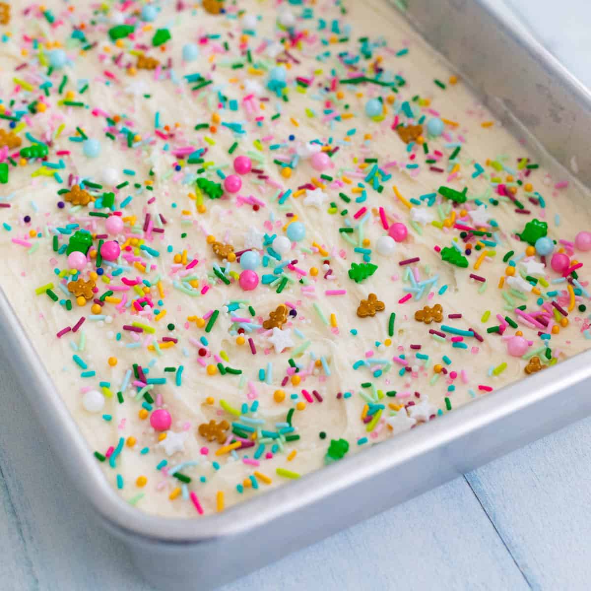 A pan of sugar cookie bars have been decorated with the vanilla frosting and festive red, green, and pink sprinkles.