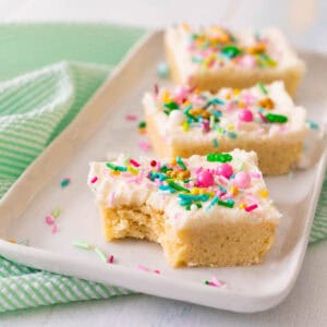 A white platter has 3 sugar cookie bars with white frosting and colorful sprinkles on top.