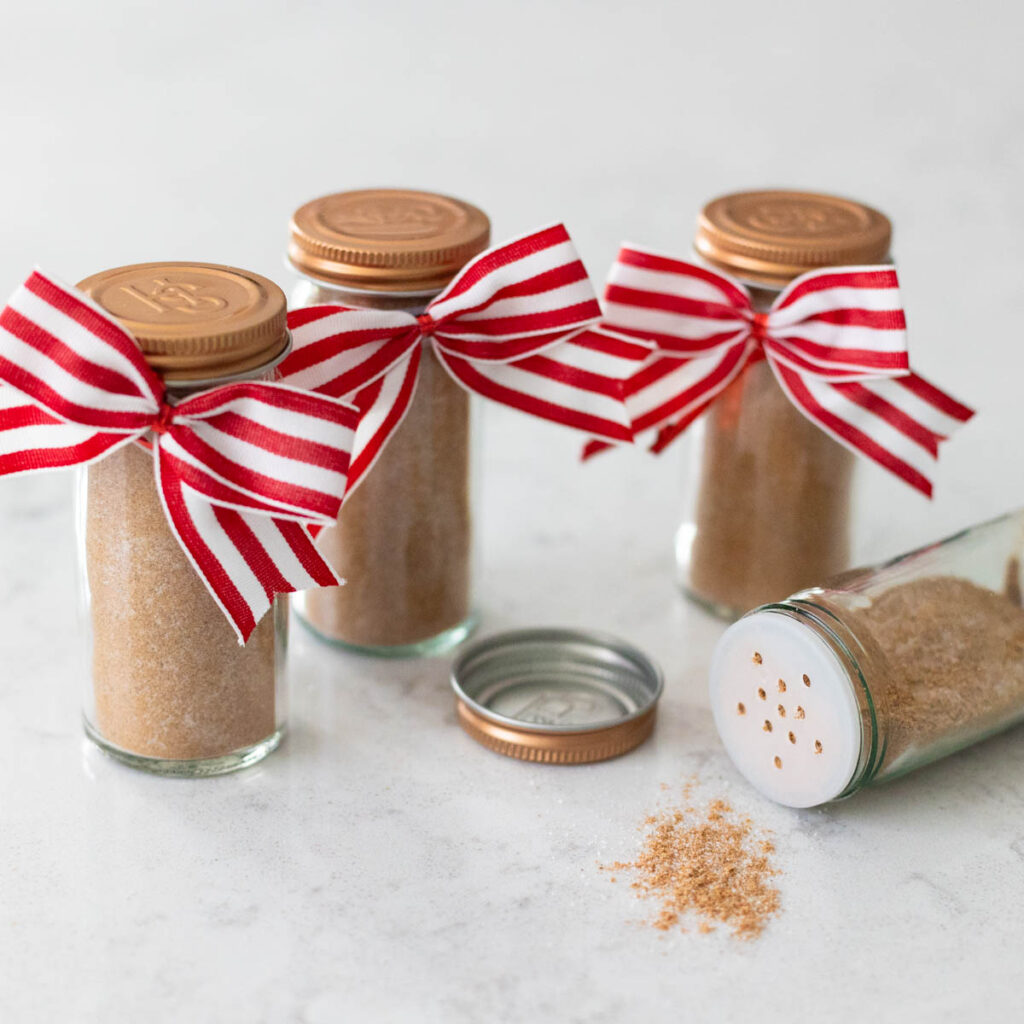 4 jars of the homemade spice mix have red and white bows for gifting. One jar is on its side with some spice spilling out.
