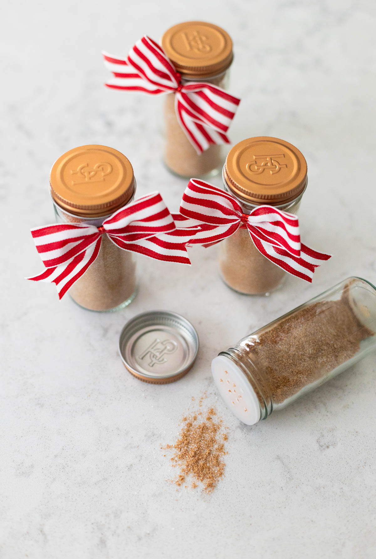 4 jars of the homemade spice mix have red and white bows for gifting. One jar is on its side with some spice spilling out.