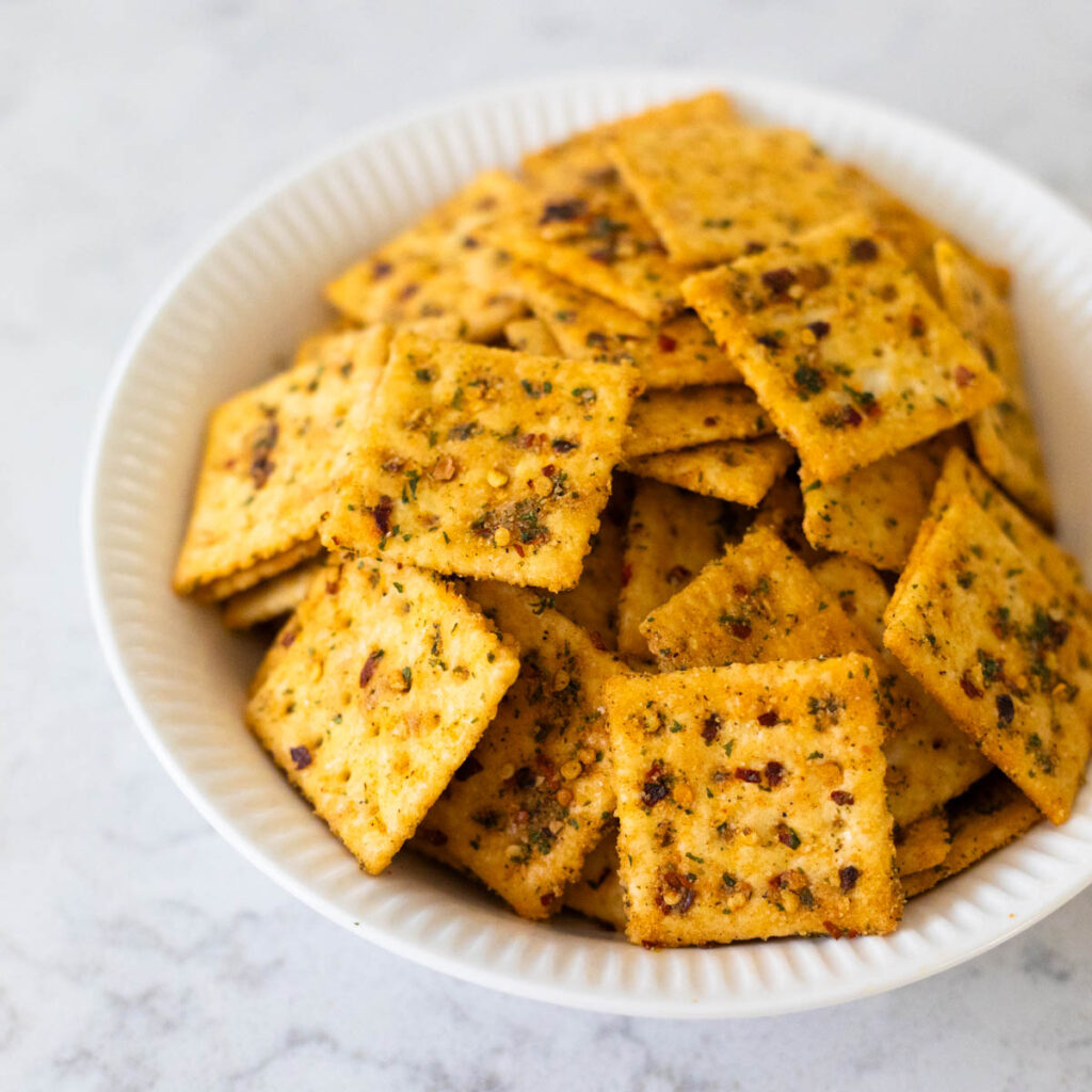 A white bowl is filled with seasoned saltine crackers.