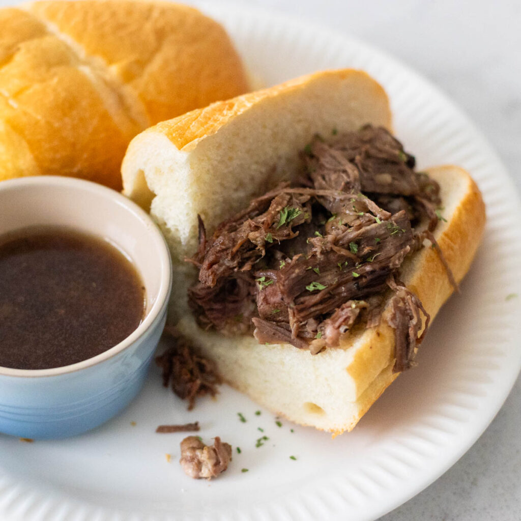 A hearty beef sandwich sits next to a cup of beef au jus dipping sauce.