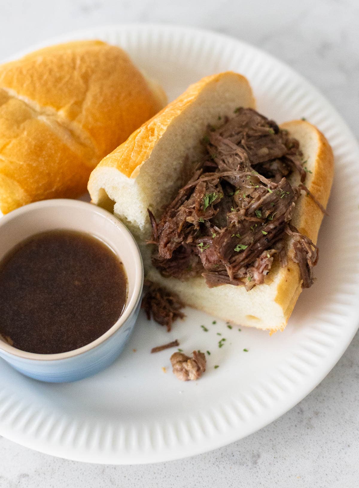 A hearty beef sandwich sits next to a cup of beef au jus dipping sauce.