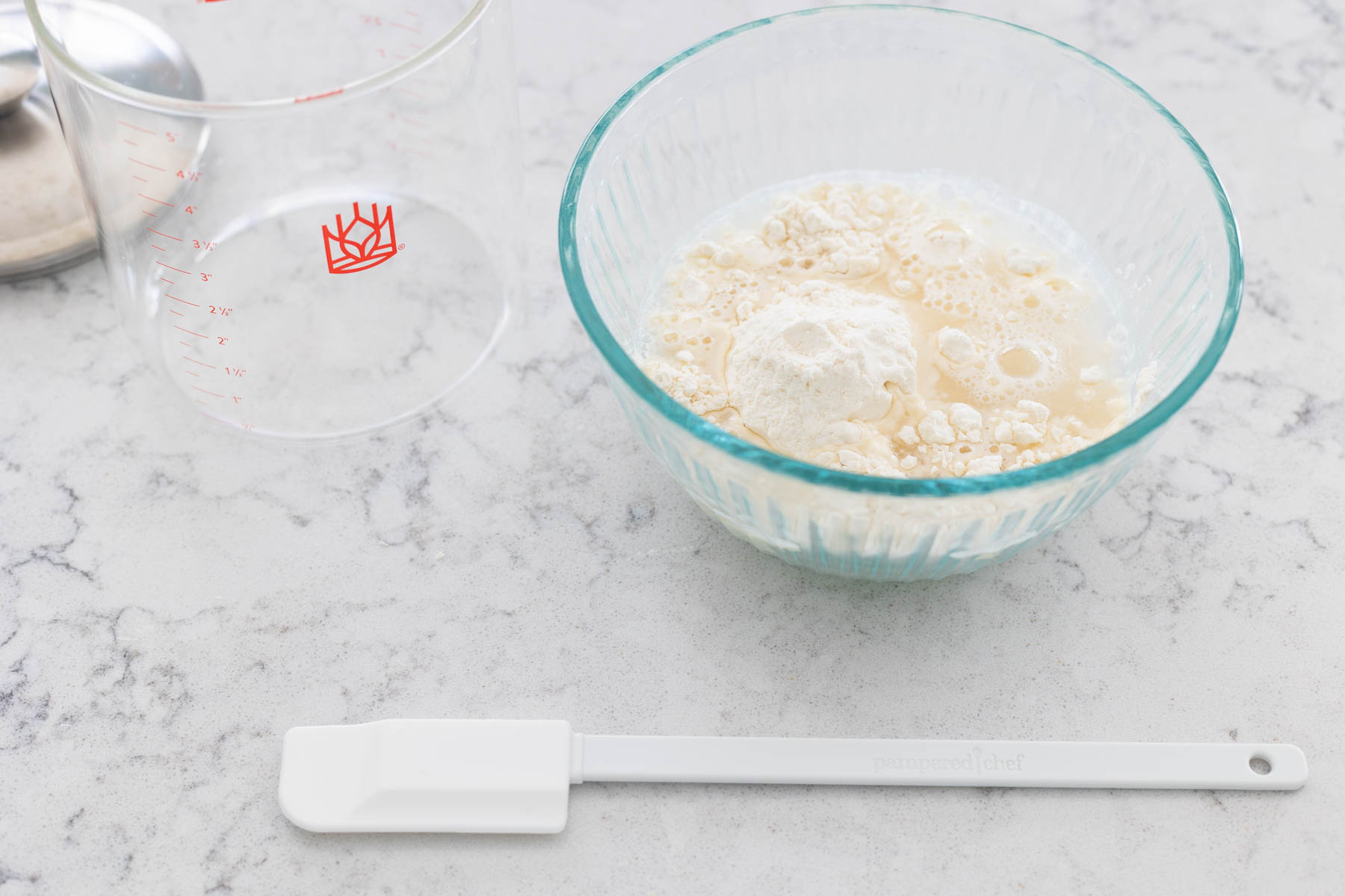 The water and flour have been added to the bowl. The spatula is about to stir them in.