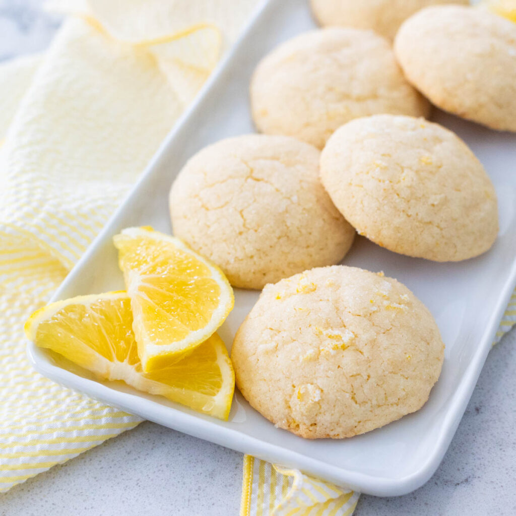 A platter of puffy lemon doodle cookies has sliced fresh lemons on the side.