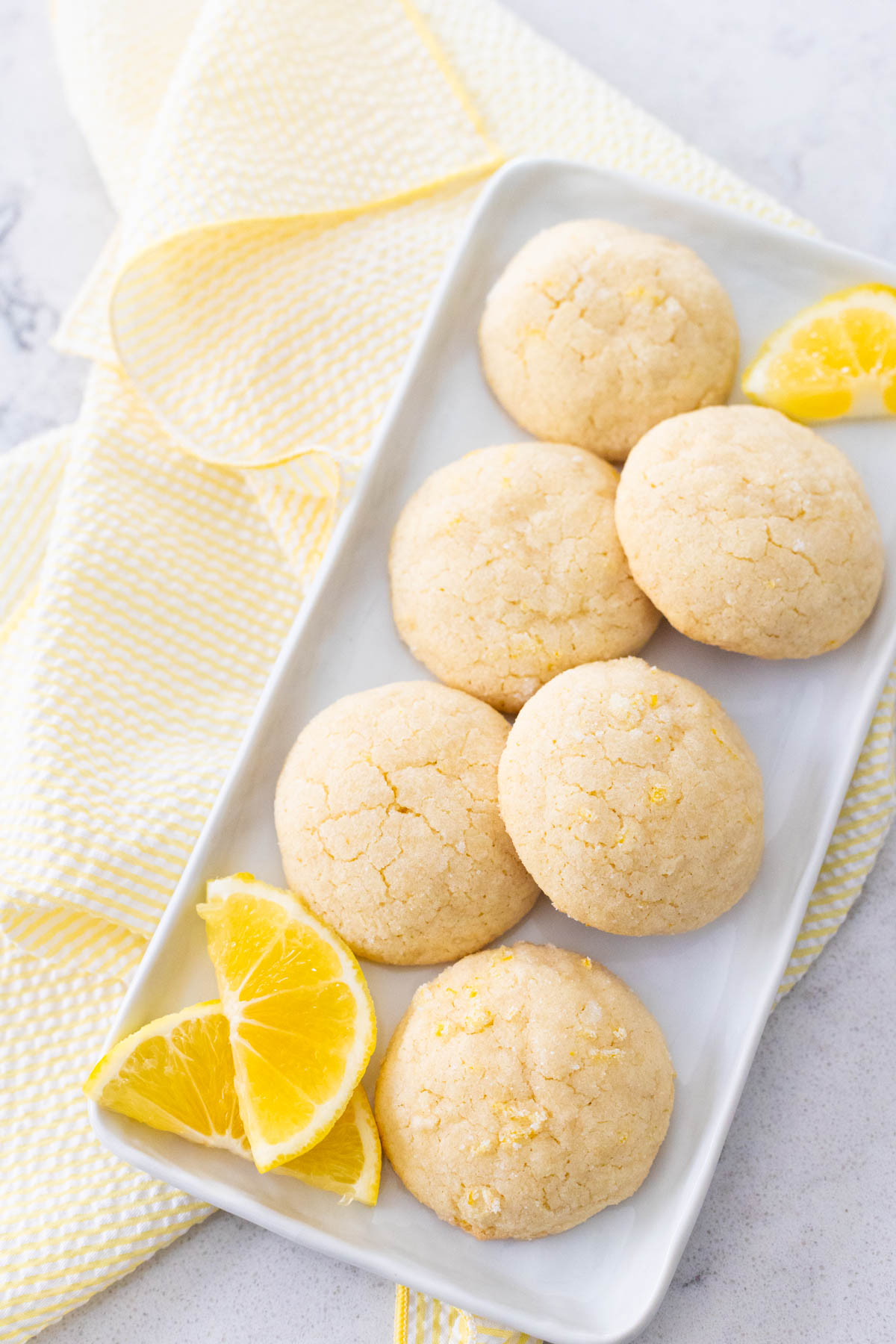 A platter of puffy lemon doodle cookies has sliced fresh lemons on the side.