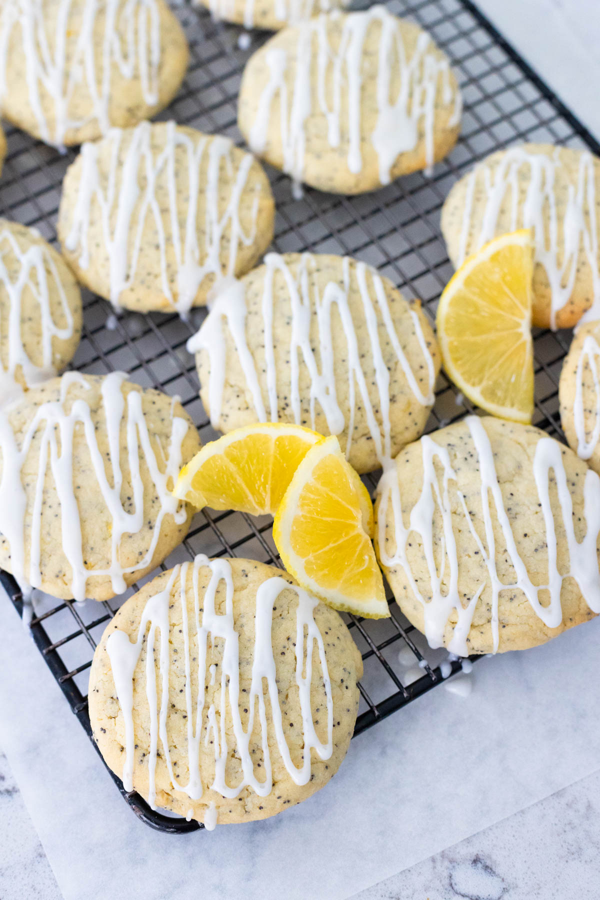 The lemon cookies are cooling on a baker's rack, they have a lemon icing drizzle over the top and fresh lemon slices on the side.