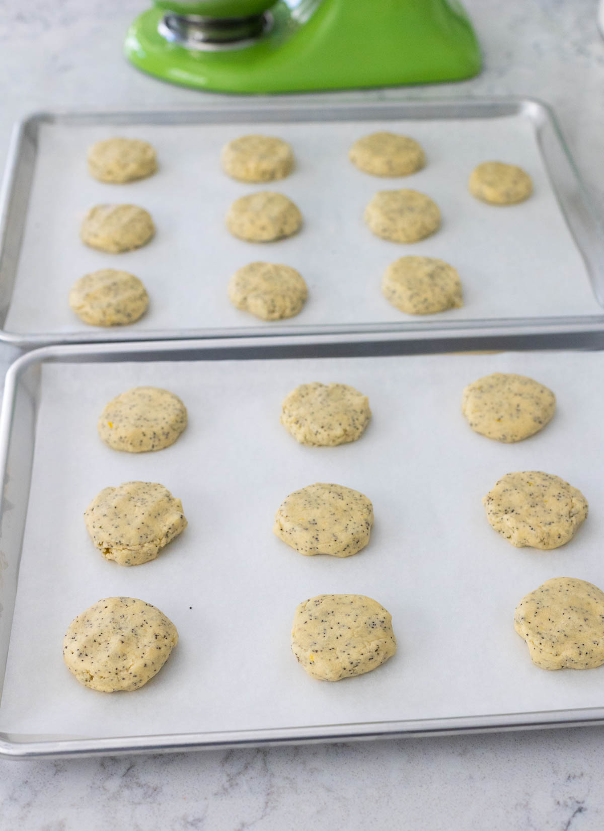 The lemon poppy seed cookies have been arranged on two baking sheets lined with parchment paper.