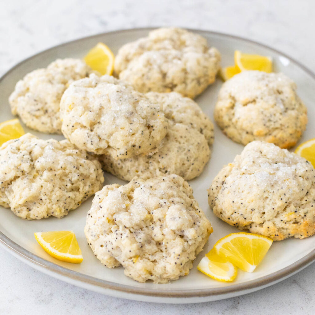 A plate of lemon scones with sugared topping has sliced lemons on the side.