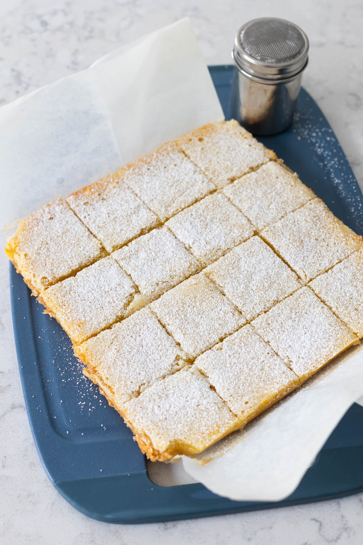 The bars have come out of the oven, cooled, and then pulled out of the pan by the parchment paper. The bars are cut into squares.