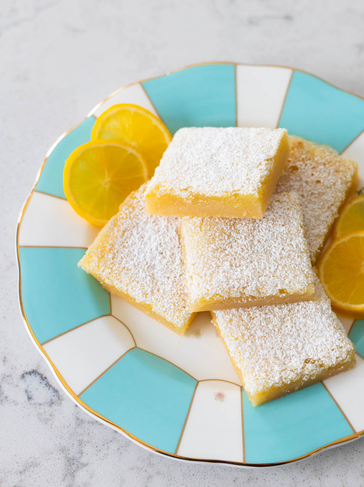 A plate of lemon bars has one square in front that has a bite taken out of it.