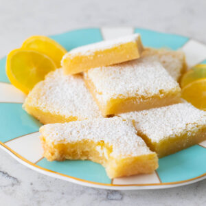 A plate of lemon bars has one square in front that has a bite taken out of it.