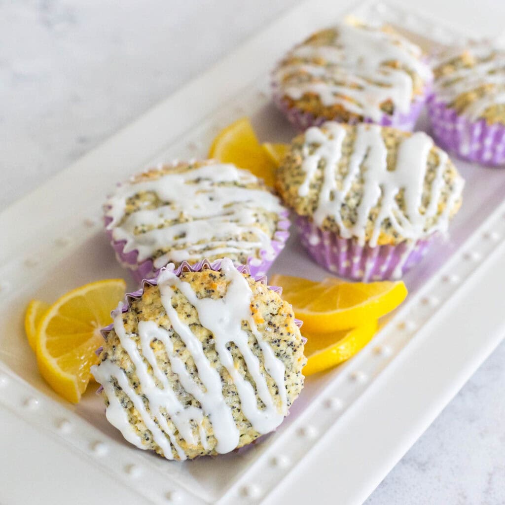 A platter of glazed muffins has fresh lemon wedges on the side.