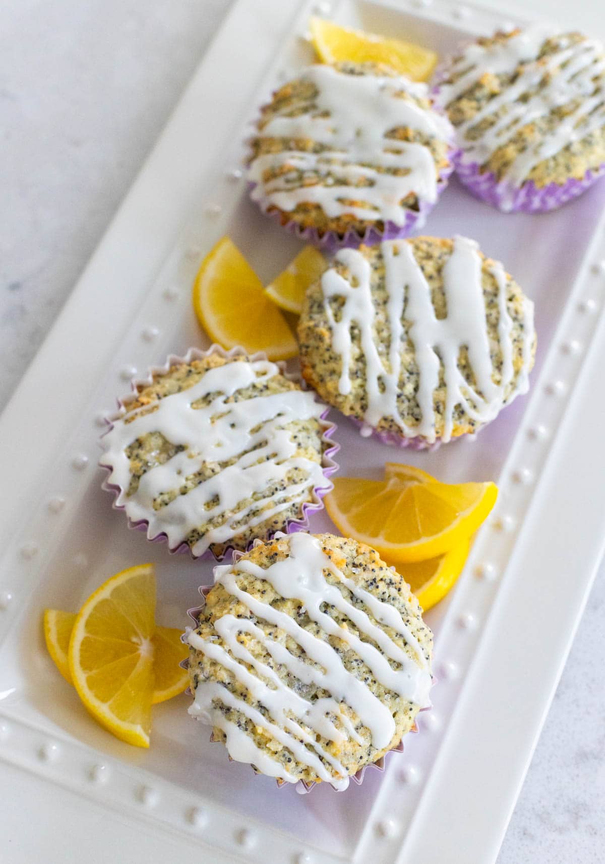 A platter of glazed muffins has fresh lemon wedges on the side.
