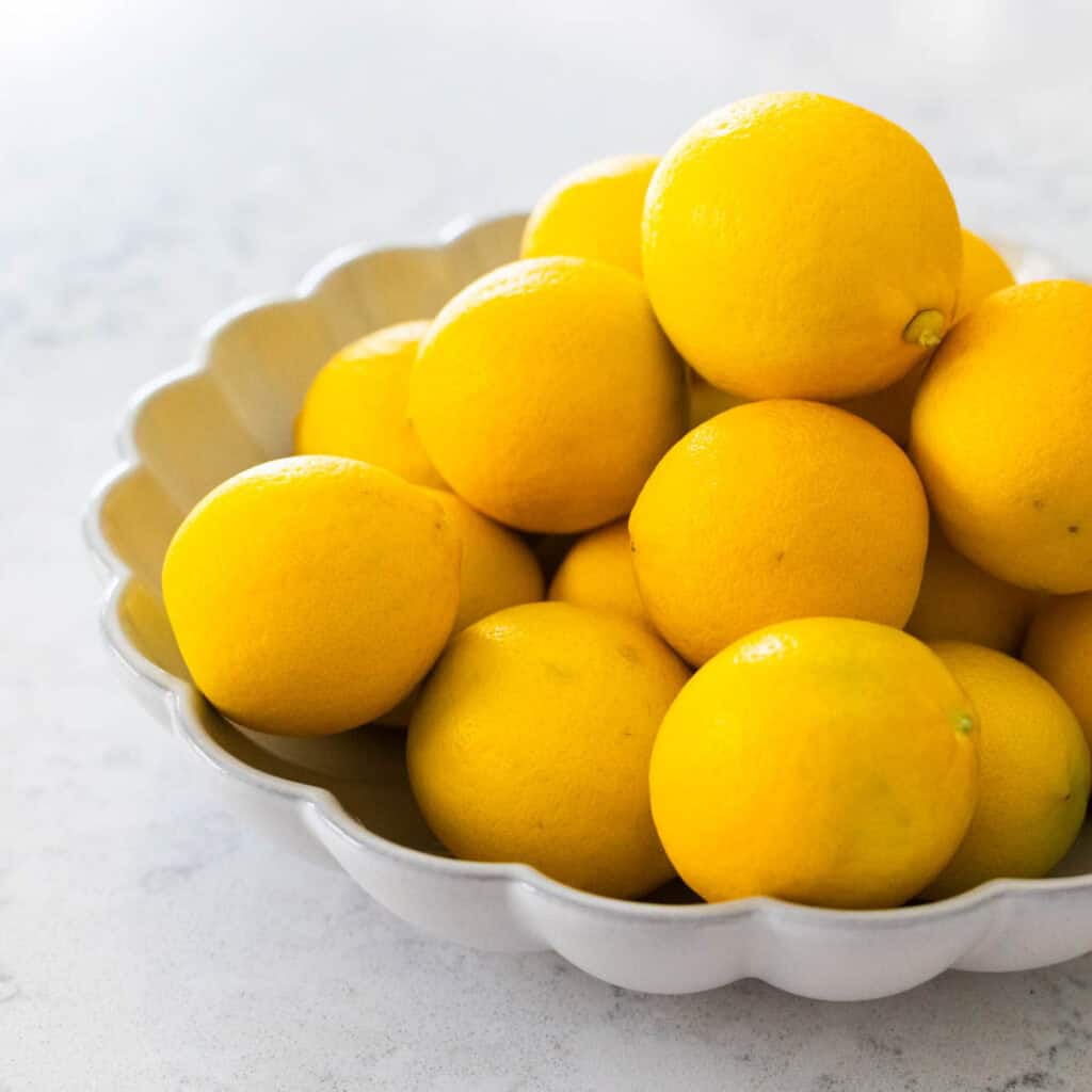 A scalloped bowl is filled with a pile of Meyer Lemons.